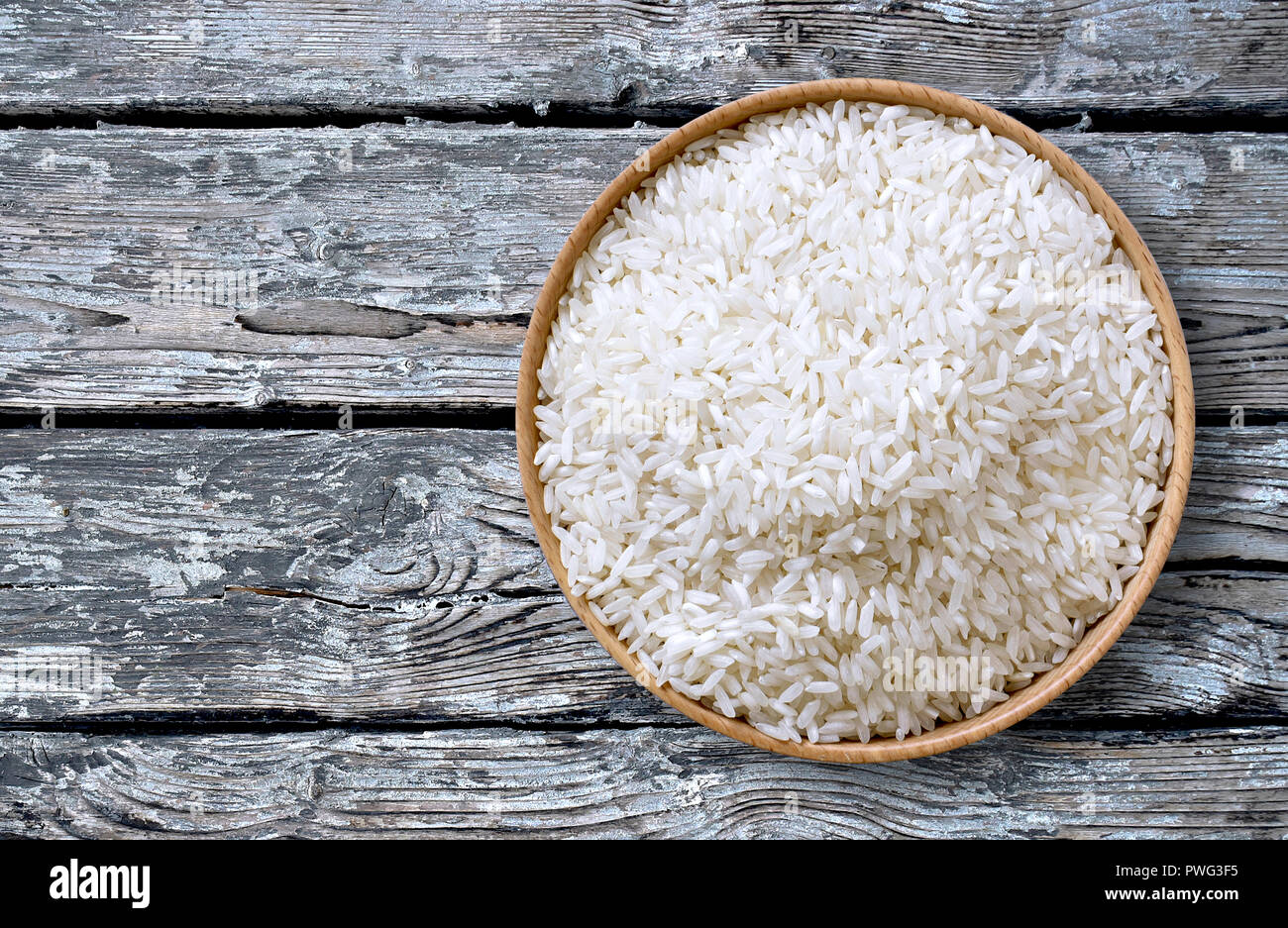 Healthy eating scene with raw, parboiled rice in a wooden bowl, top view or closeup shot on a weathered wooden table. Stock Photo