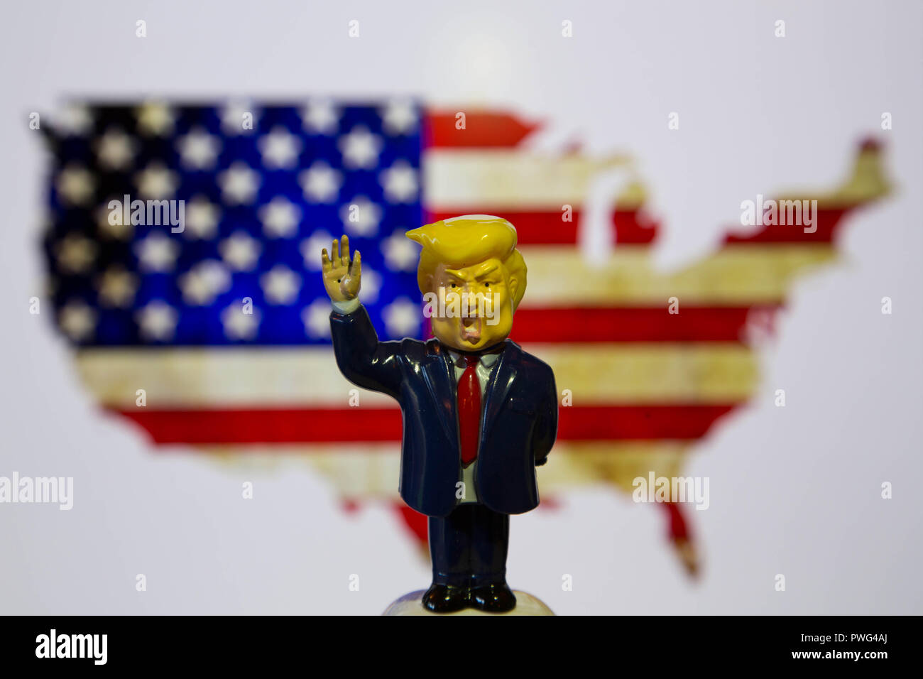 Trump bobblehead standing in front of American flag in shape of USA with hand rasied. Stock Photo