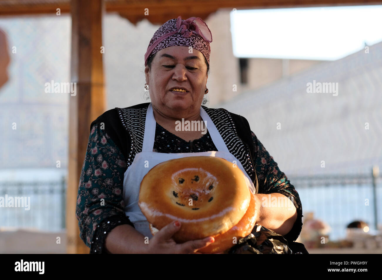 A vendor with capped gold teeth selling traditional Bukhara-style non or naan oven-baked flatbread in Siyob Bazaar also called Siab Bazaar, the largest bazaar in the city of Samarkand alternatively Samarqand in Uzbekistan. Replacing natural teeth with gold implants or caps was once a status symbol and prestige in Uzbekistan and other countries of Central Asia. However, the younger generation seldom follows this tradition. Stock Photo