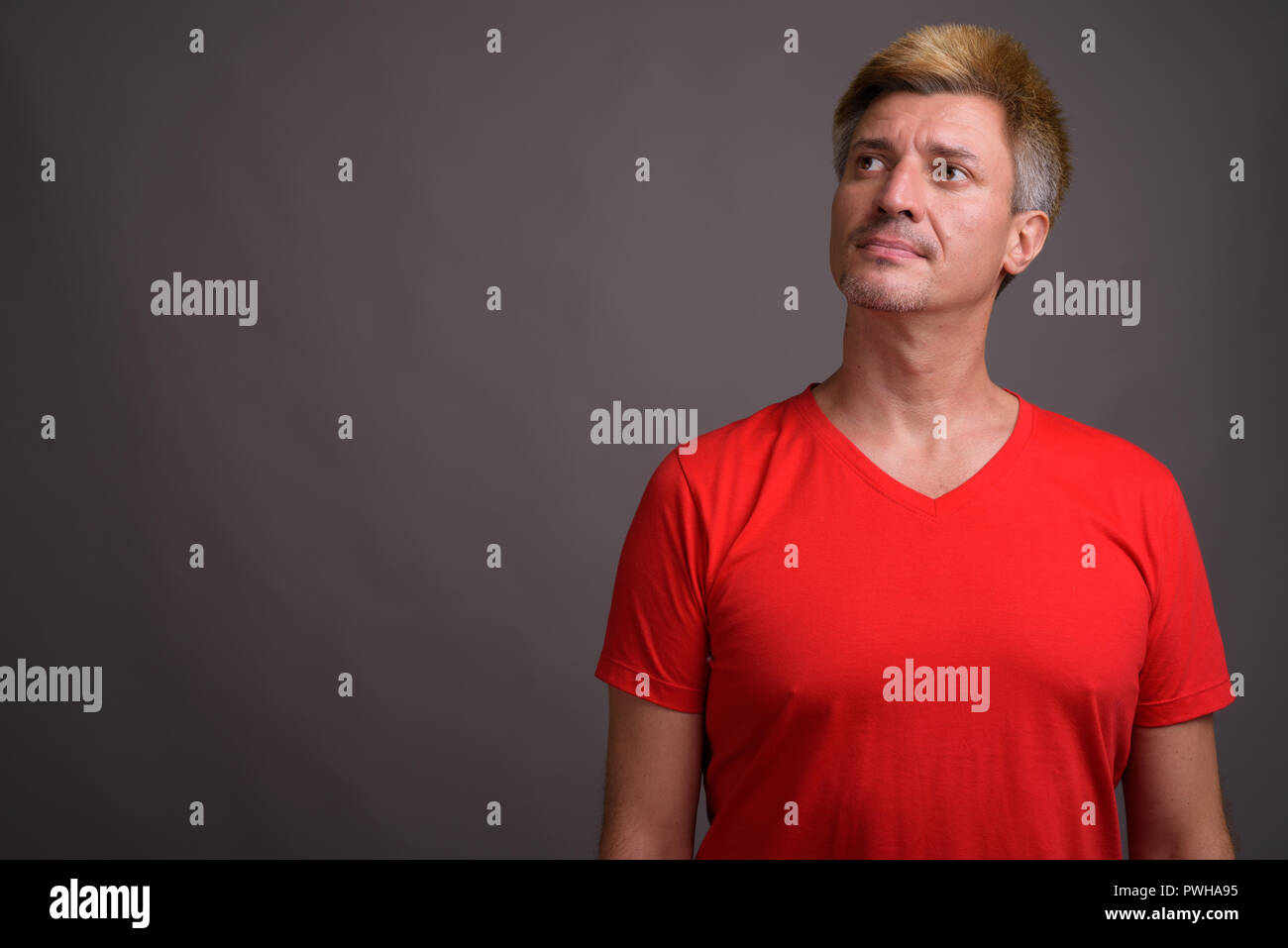 Man with blond hair wearing red shirt against gray background Stock Photo