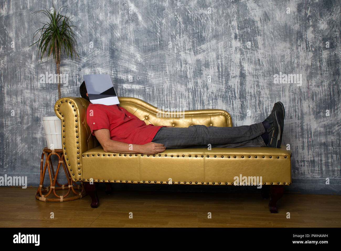 man lying sleeping on golden leather couch with a magazine on his face