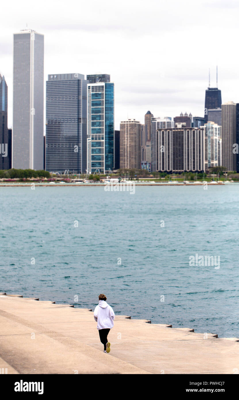 Female runner by Michigan lake in a cold cloudy day.  Chicago skyline in the background. Picture taken at Chicago Lakefront close to Adler Planetarium Stock Photo