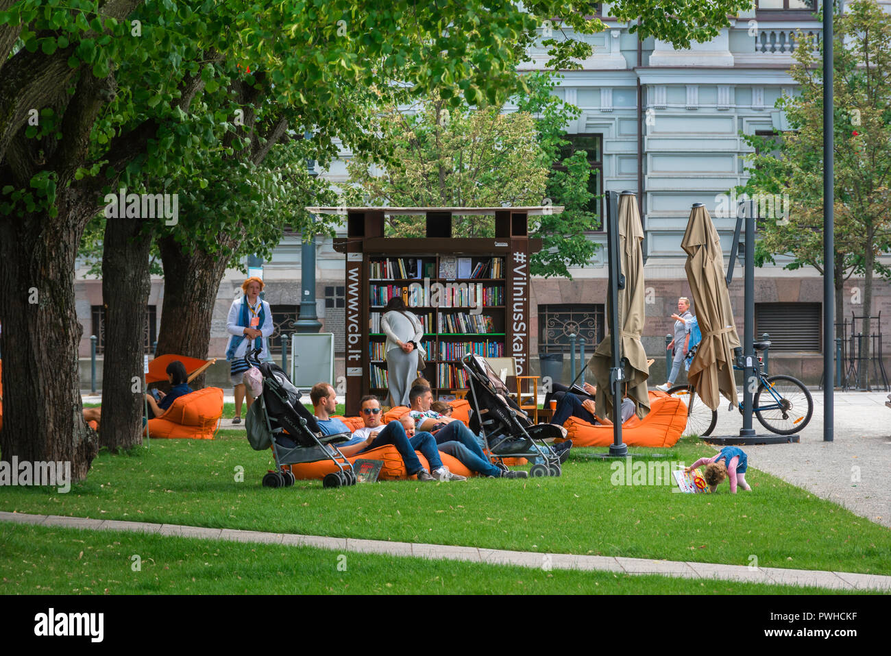 Lithuania people park, view of a family group relaxing near a courtesy bookstand in a corner of Lukiskiu aikste city park in the Vilnius New Town area. Stock Photo
