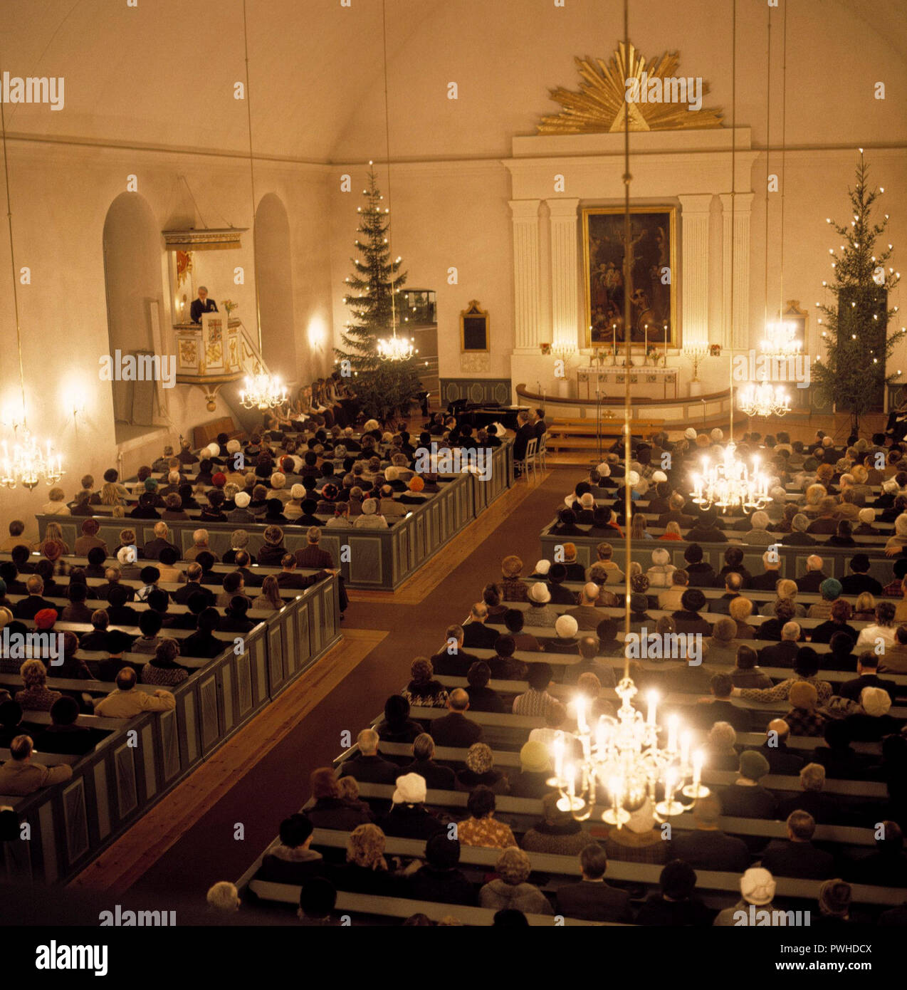 Early service on Christmas day. Interior from a church where people are sitting listening to the priest. The church is decorated with christmas trees. Sweden 1970s Stock Photo