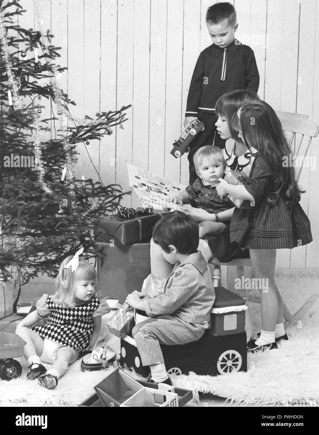 Christmas in the 1960s. Children in diffent ages in a room with at christmas tree and presents. Some presents has been opened and the children are playing with them. Sweden 1965 Stock Photo
