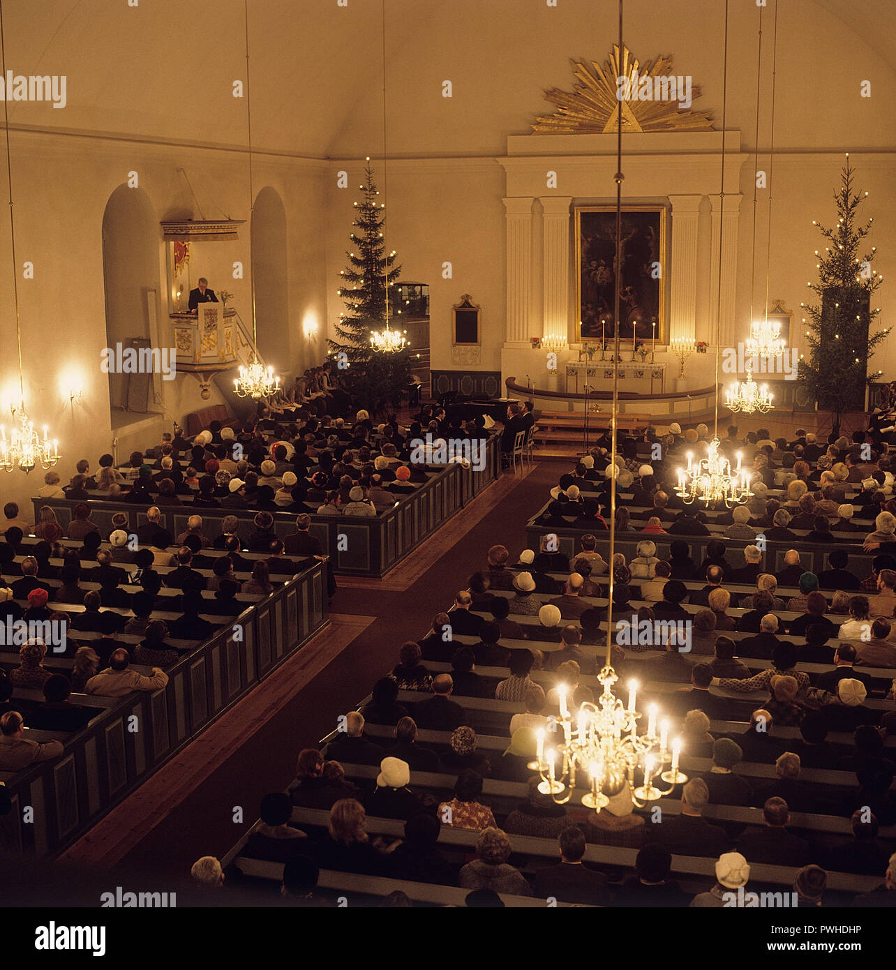 Early service on Christmas day. Interior from a church where people are sitting listening to the priest. The church is decorated with christmas trees. Sweden 1970s. Stock Photo