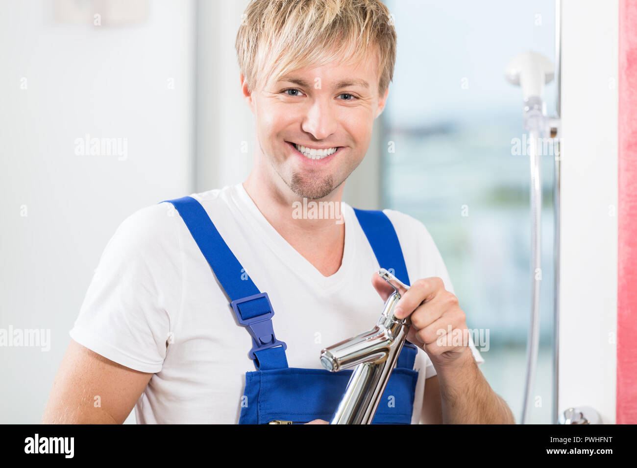 Portrait of a cheerful maintenance worker holding a faucet in a Stock