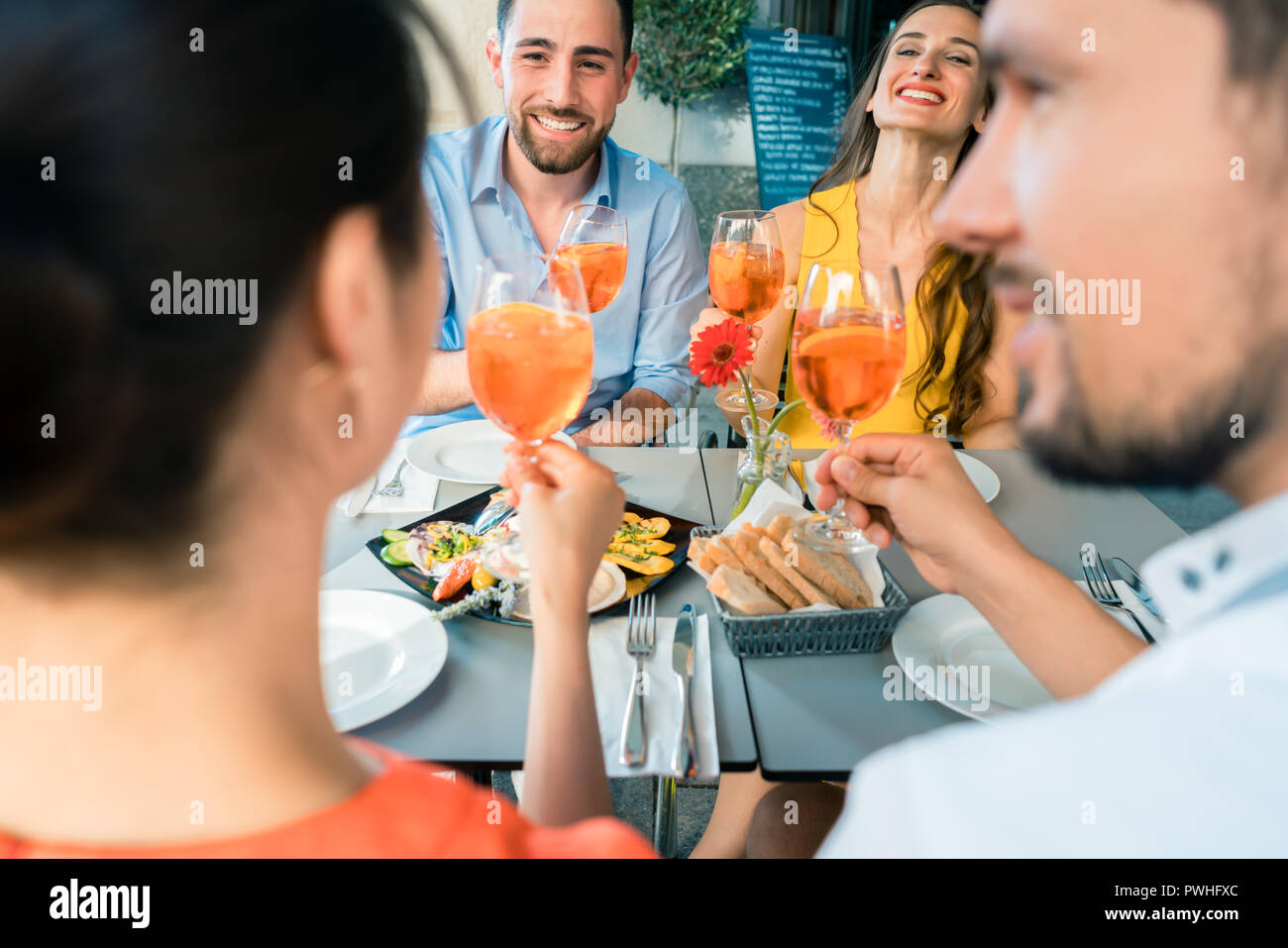 Two happy young couples toasting while sitting together at resta Stock Photo