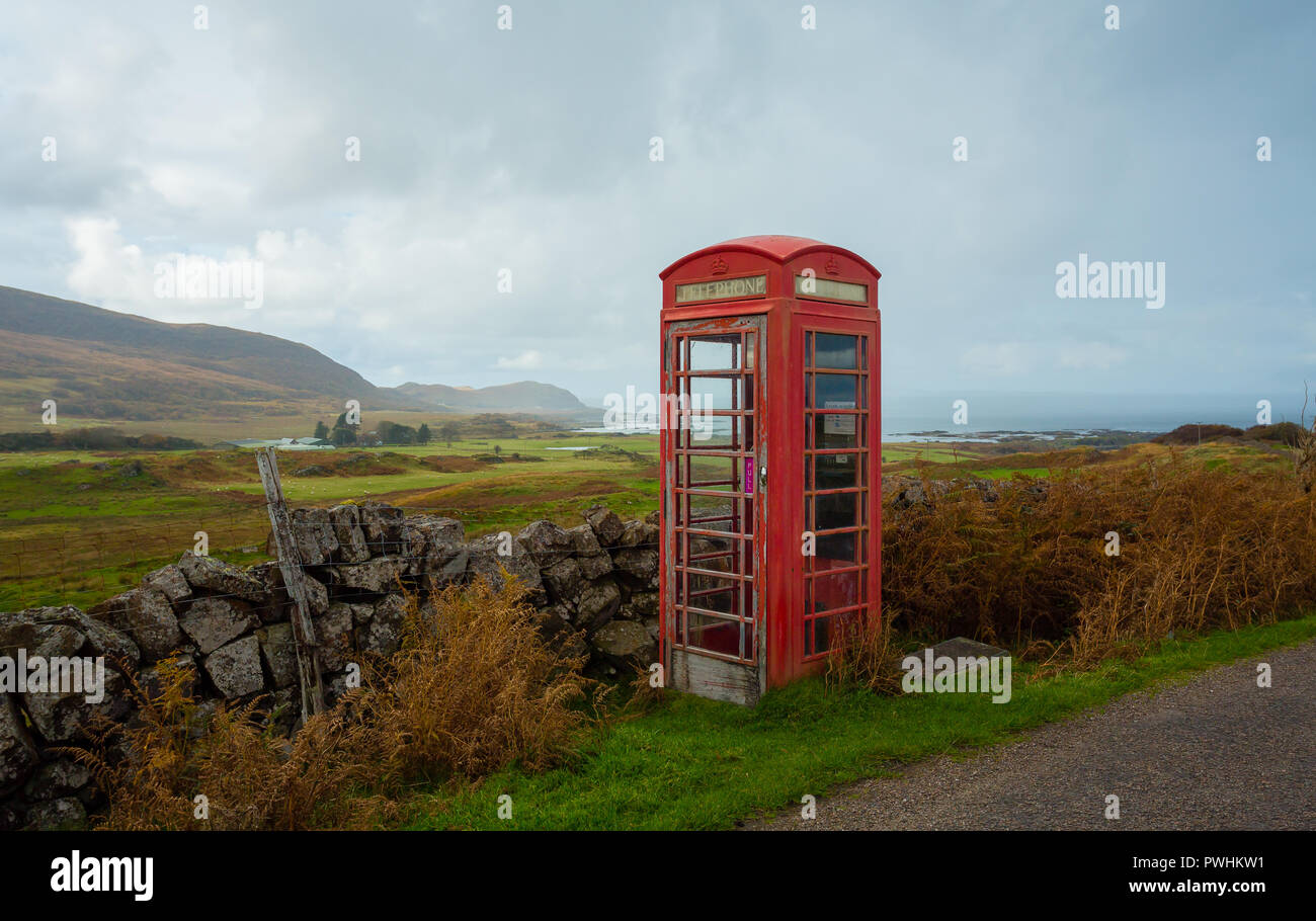 Old fashioned red telephone box, abandoned and defunct in a rural village in the Highlands of Scotland overlooking the Hebridean isle of Eigg. Stock Photo