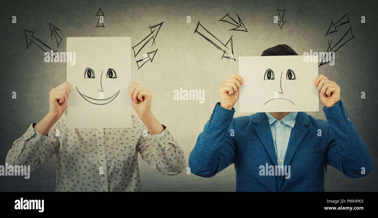 Businessman and businesswoman covering their faces using sheets with drawn happy and sad emoticons, like a mask to hide her real emotion from society. Stock Photo