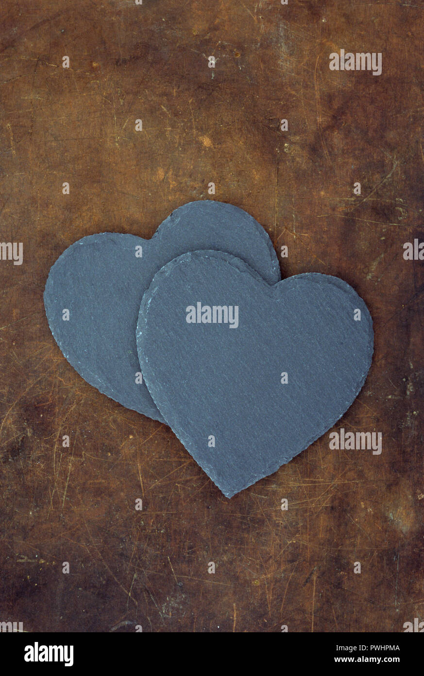 Two heart shaped pieces of grey slate lying on worn brown leather Stock Photo