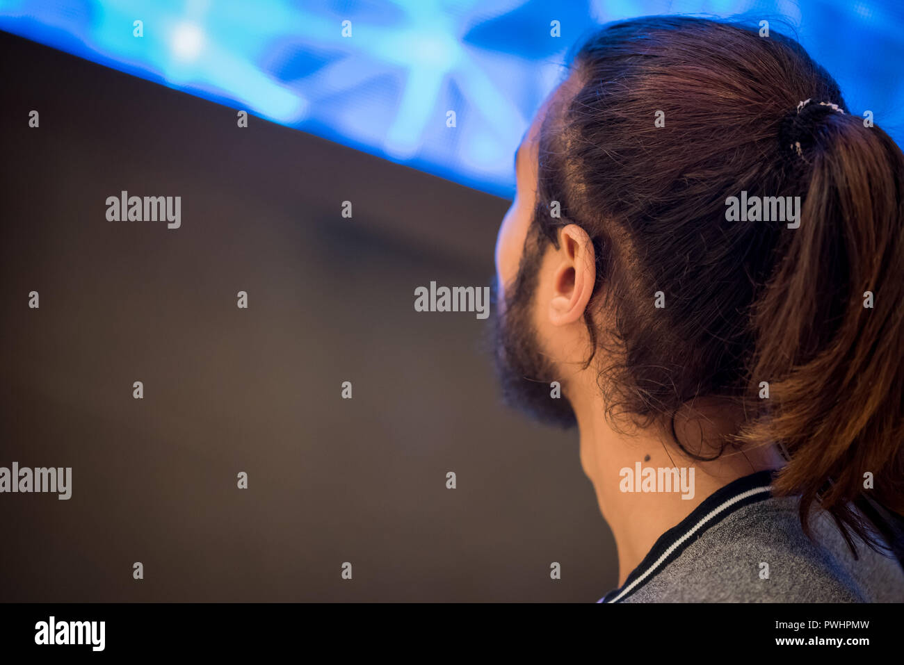 Sep 23, 2018: A young boy with long hair and wearing pony looking away at screen, Abu Dhabi, UAE Stock Photo