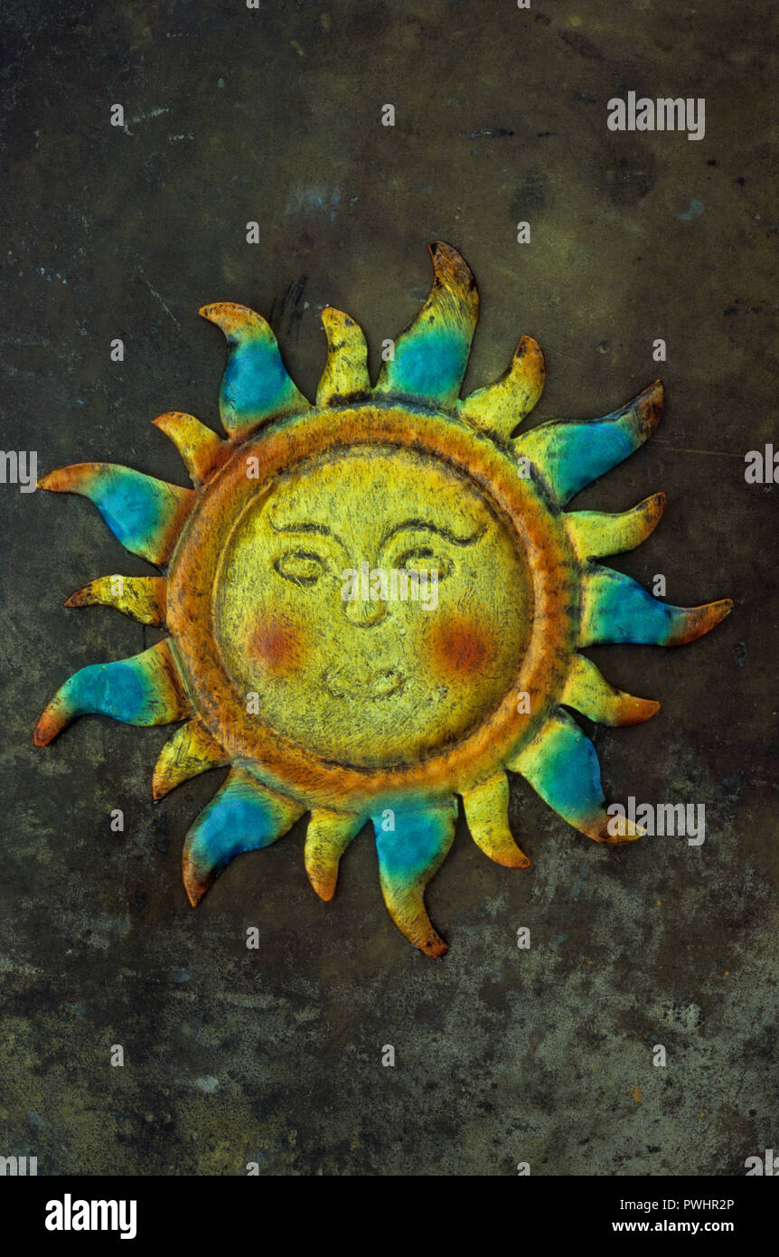 Tin model of sun with yellow face glowing cheeks and orange and blue rays lying on tarnished brass Stock Photo