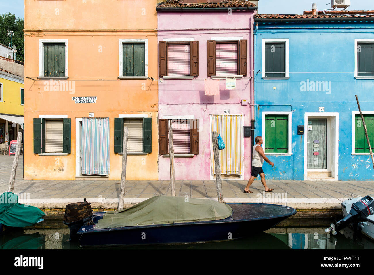 A man walks past a row of colourful houses by the canal in Burano, Venice, Italy Stock Photo