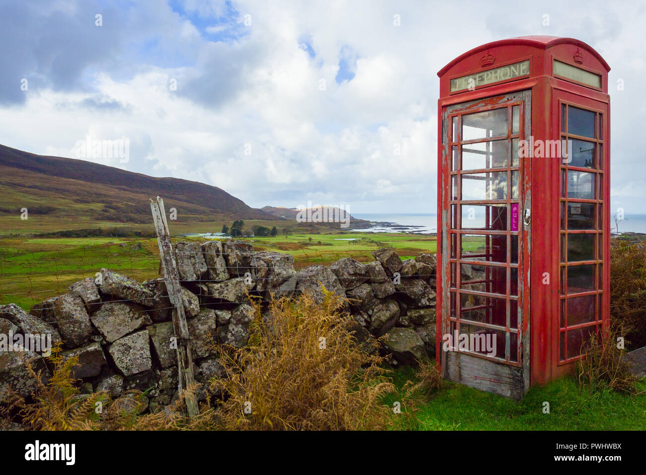 Old fashioned red telephone box, abandoned and defunct in a rural village in the Highlands of Scotland overlooking the Hebridean isle of Eigg. Stock Photo
