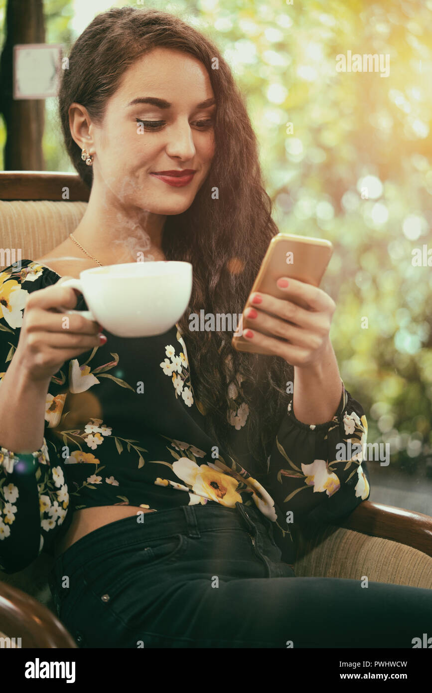 Young woman drinking coffee and using her phone at the coffee shop Stock Photo