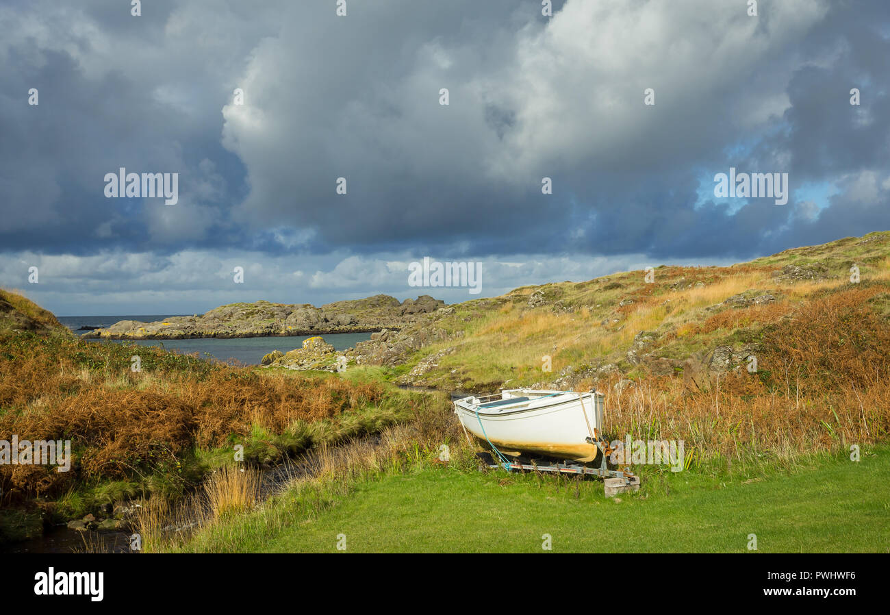 Scotland, small white fishing boat tied up on dry land in remote area of the Ardnamurchan peninsular in the Scottish Highlands. Heavy, cloudy skies. Stock Photo