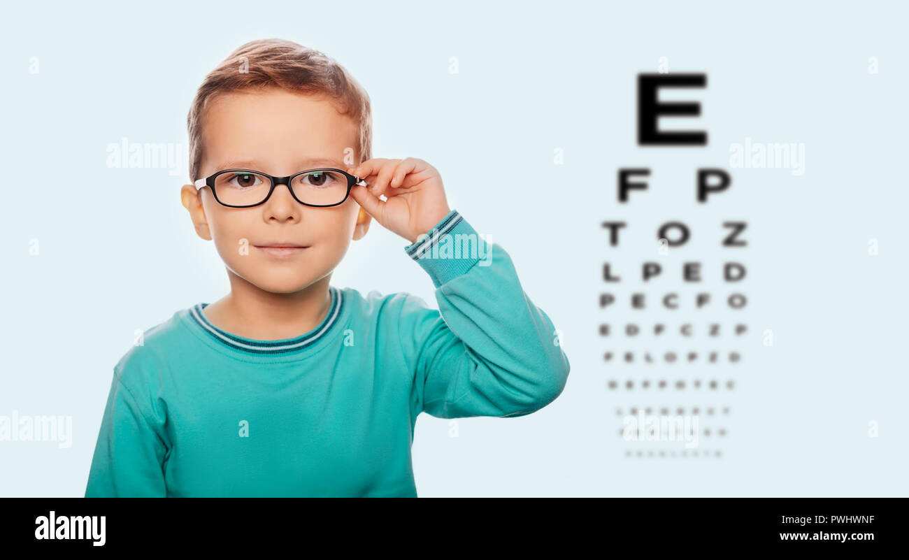 Little boy adjusting his new eyeglasses, on the eye chart background. Vision correction for children Stock Photo