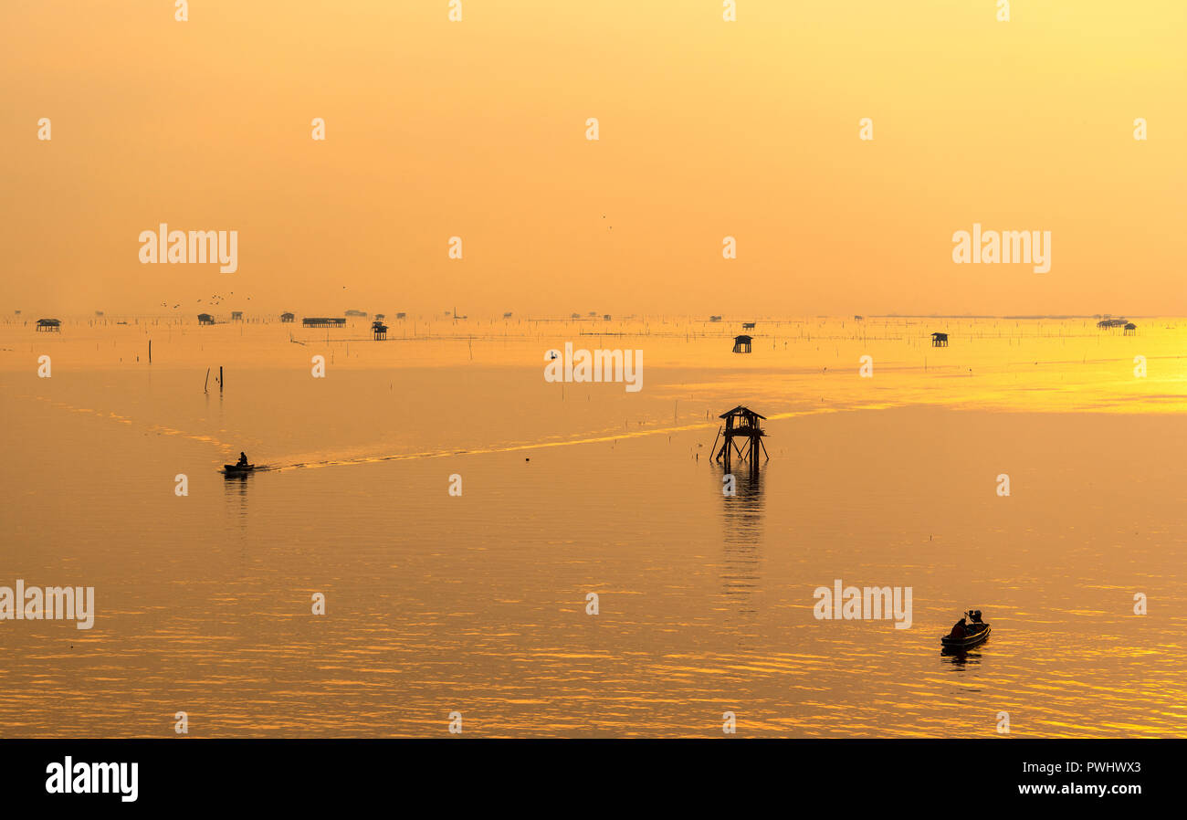 Silhouette of fisherman with his boat in the sea during sunrise. Stock Photo
