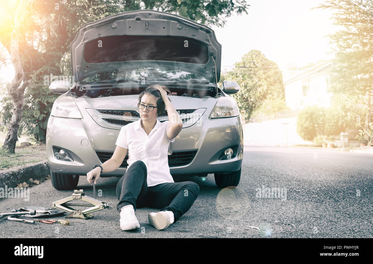 Woman sitting on ground near her car broken down on the road side. Stock Photo