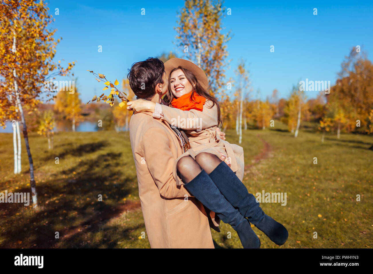 Young couple walks in autumn forest. Man carrying his girlfriend in hands and laughing. Romantic date Stock Photo