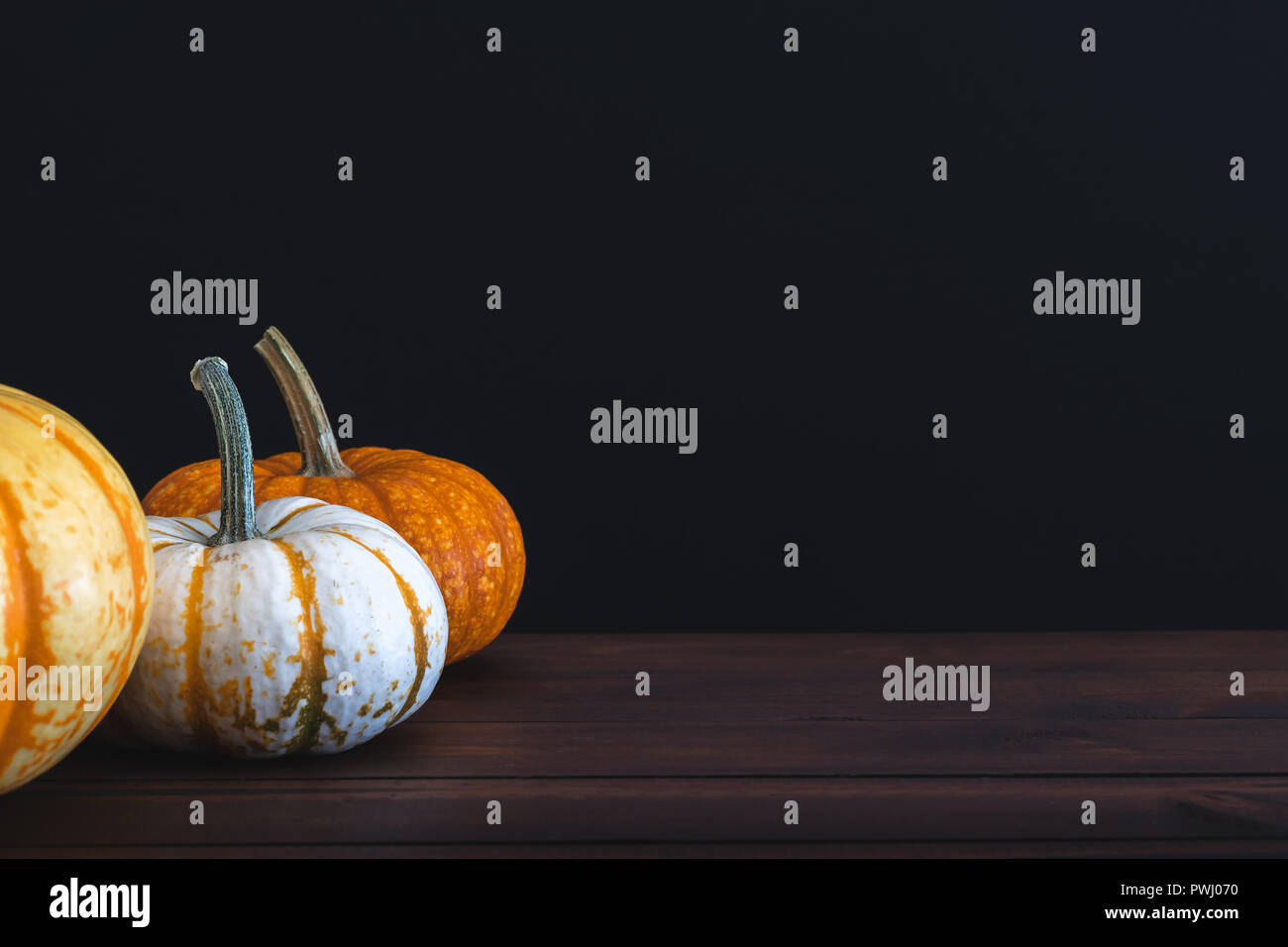 Multiple pumpkins on brown table with black background for copy space of holiday messaging. Stock Photo