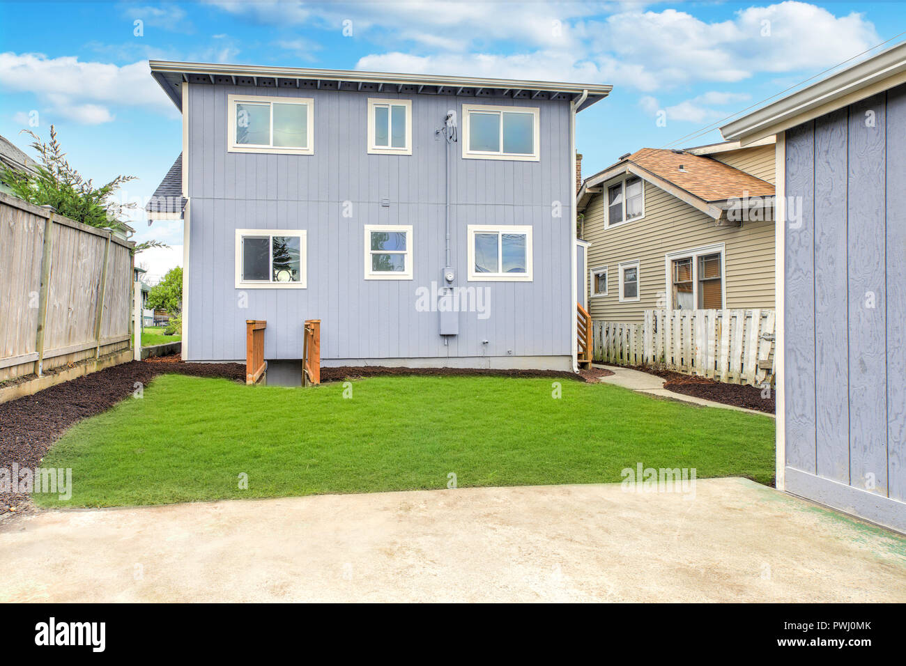 Blue home exterior with large fully fenced back yard and well kept lawn. Stock Photo