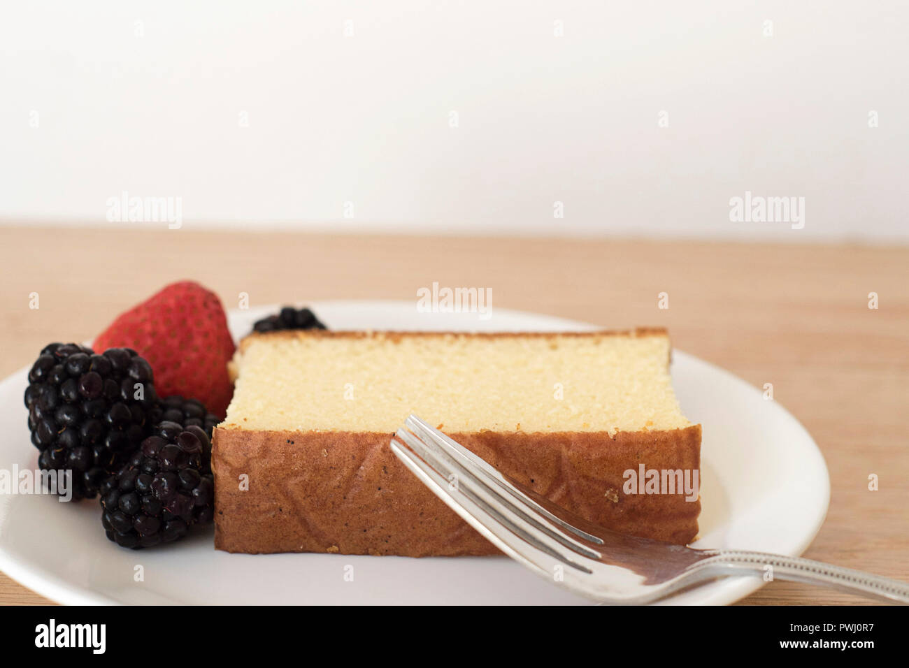 Close-up of a Single Pound Cake Slice next to some berries and a fork arranged on a plate for a snack Stock Photo