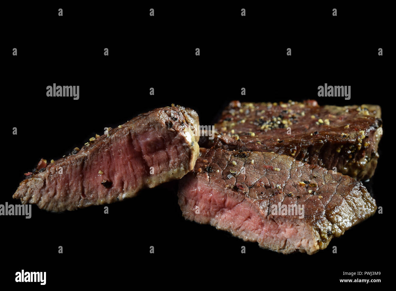 Medium rare beef steak. Spiced with peppercorns. Isolated on black. Copy space. Stock Photo