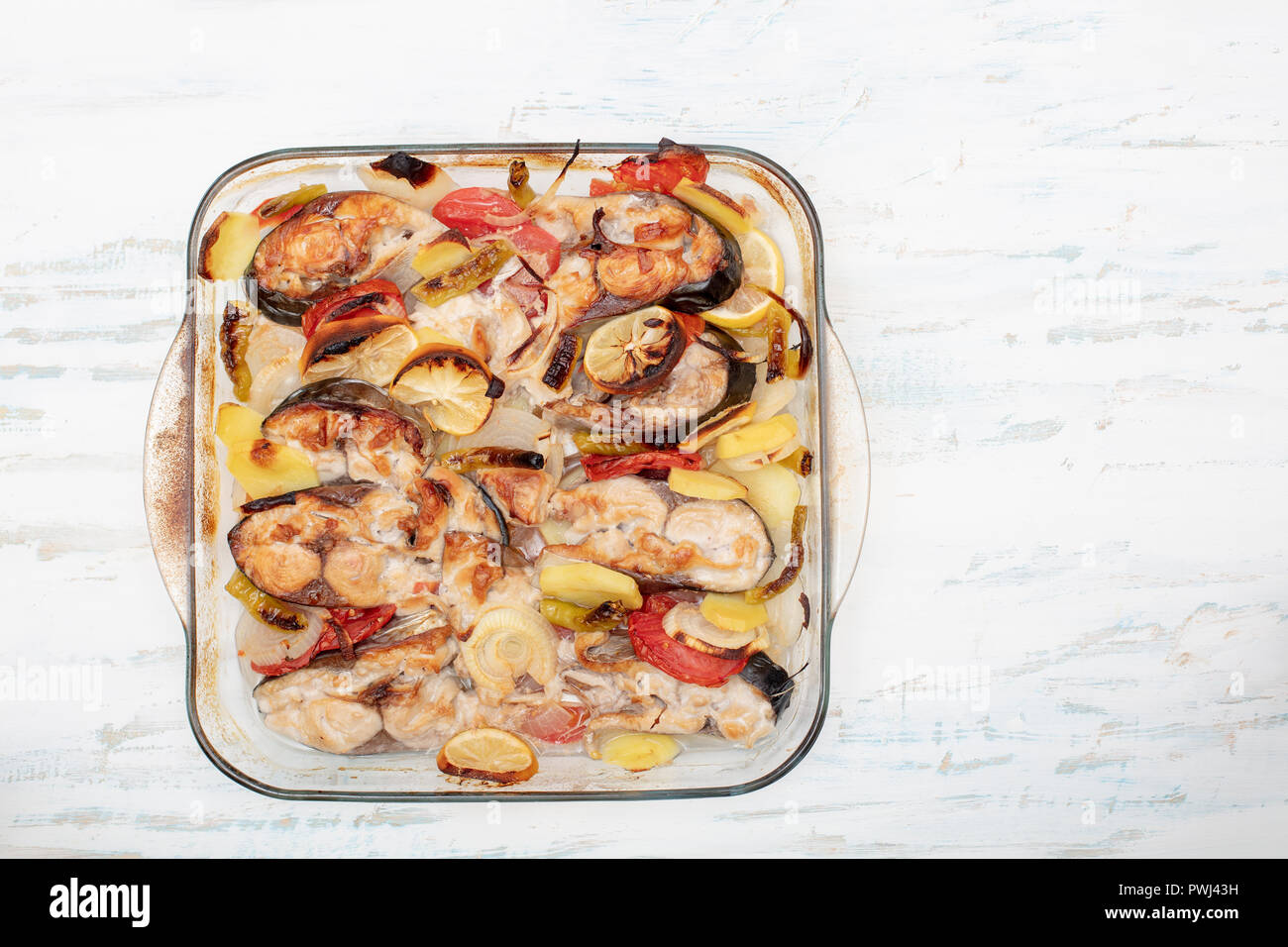 Tasty baked fish with onion, lemon, tomato and potato on glass plate on table close up Stock Photo