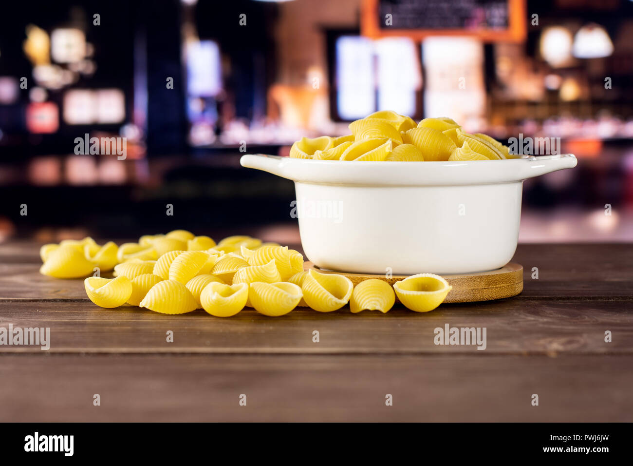 Lot of whole raw yellow pasta conchiglie variety in a ceramic stewpan with restaurant in background Stock Photo