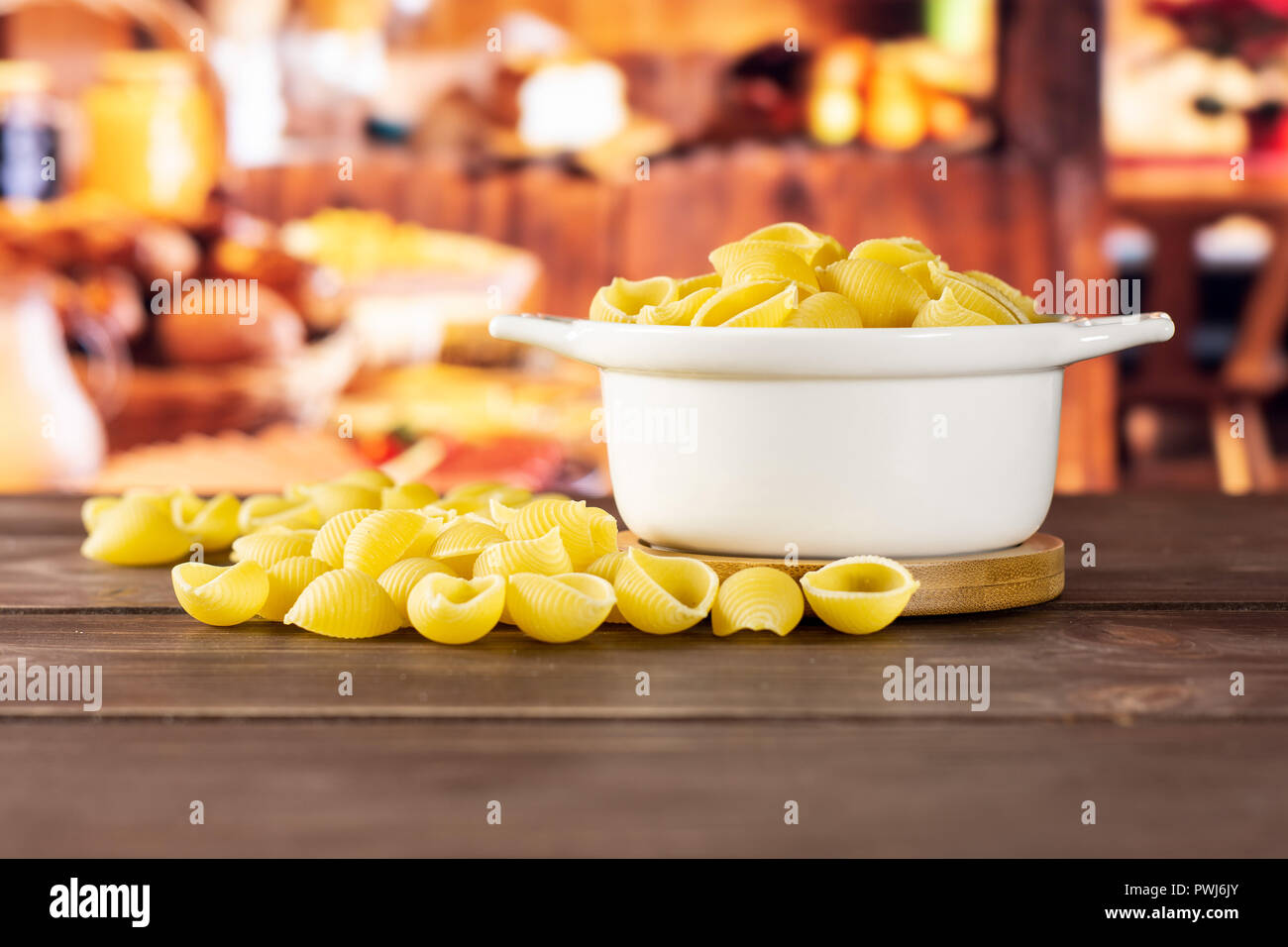 Lot of whole light raw yellow pasta conchiglie variety in a ceramic stewpan with rustic wood kitchen in background Stock Photo