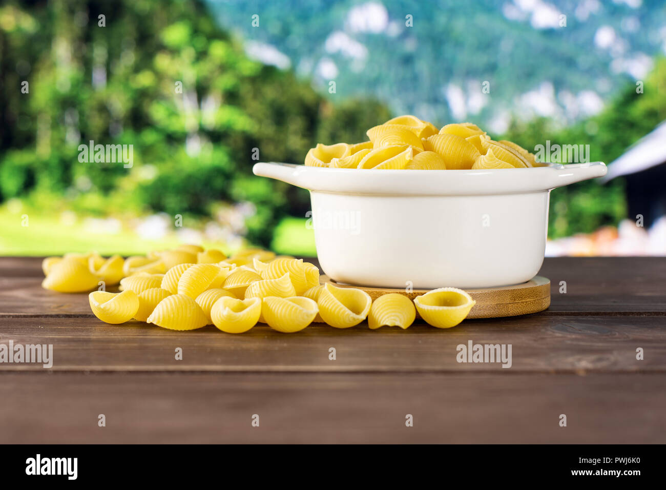 Lot of whole light raw yellow pasta conchiglie variety in a ceramic stewpan with country nature in background Stock Photo