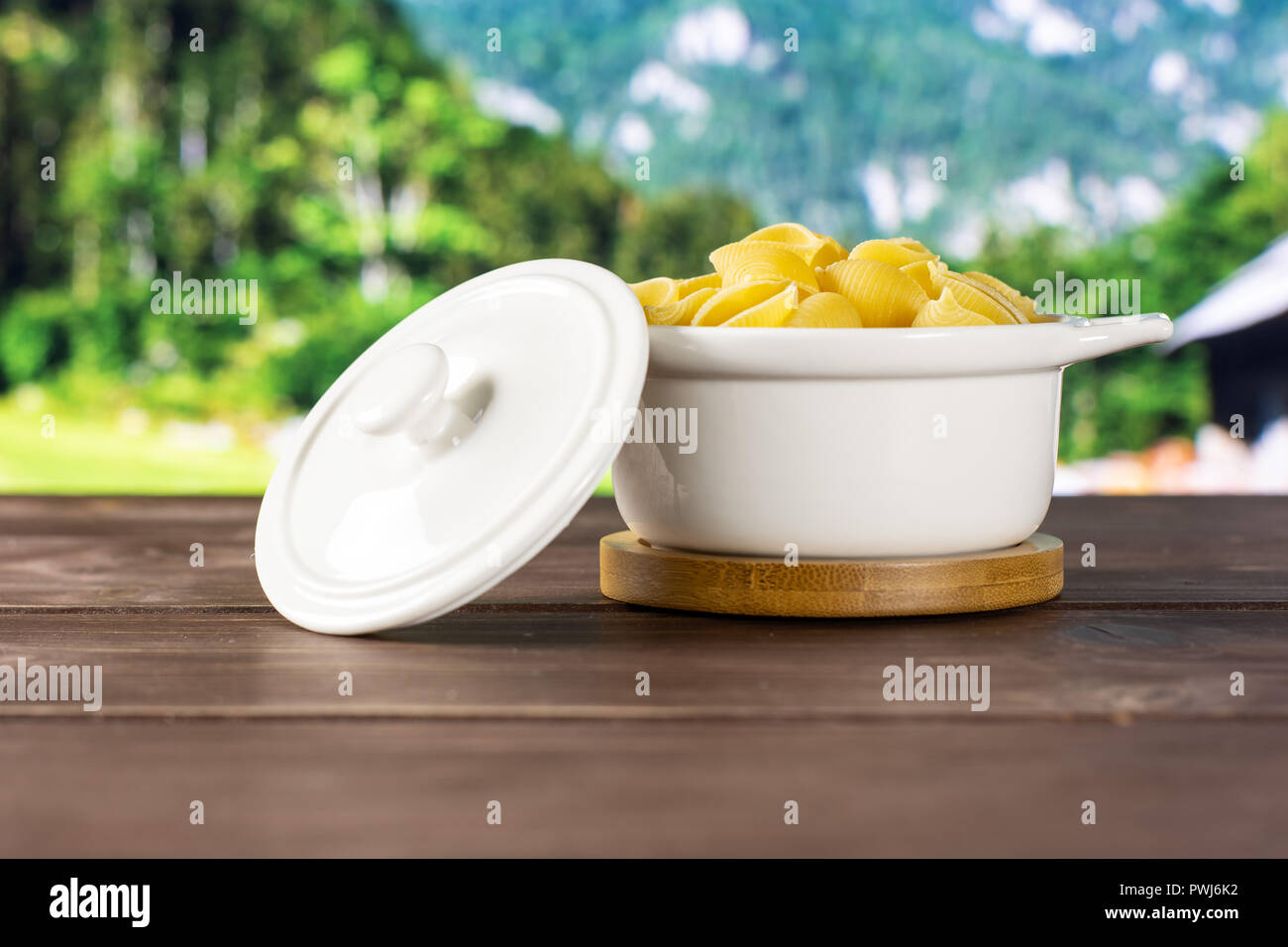 Lot of whole raw yellow pasta conchiglie variety in a ceramic stewpan with country nature in background Stock Photo