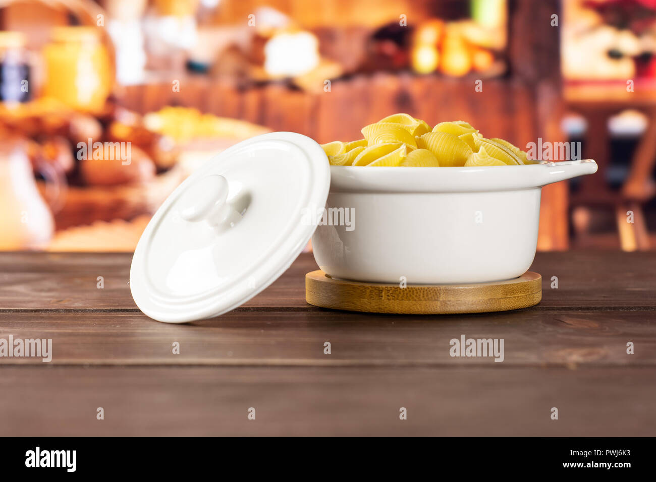 Lot of whole raw yellow pasta conchiglie variety in a ceramic stewpan with rustic wood kitchen in background Stock Photo