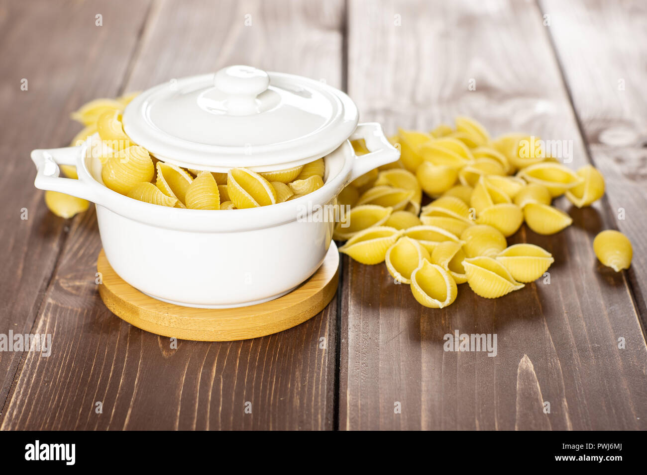 Lot of whole light raw yellow pasta conchiglie variety in a ceramic stewpan on brown wood Stock Photo