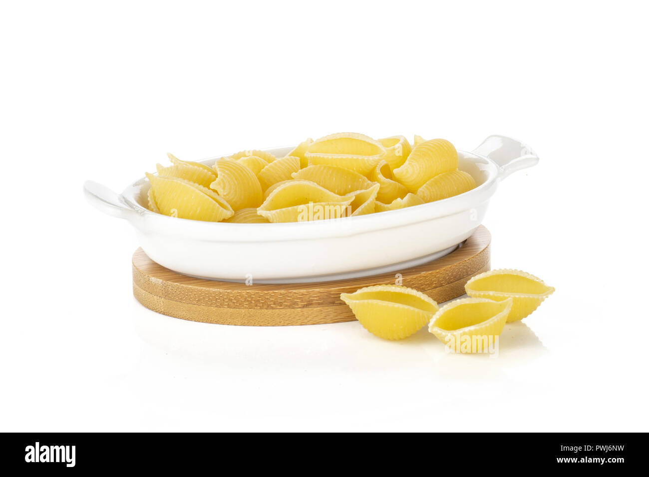 Lot of whole uncooked raw yellow pasta conchiglie variety in a ceramic stewpan isolated on white background Stock Photo