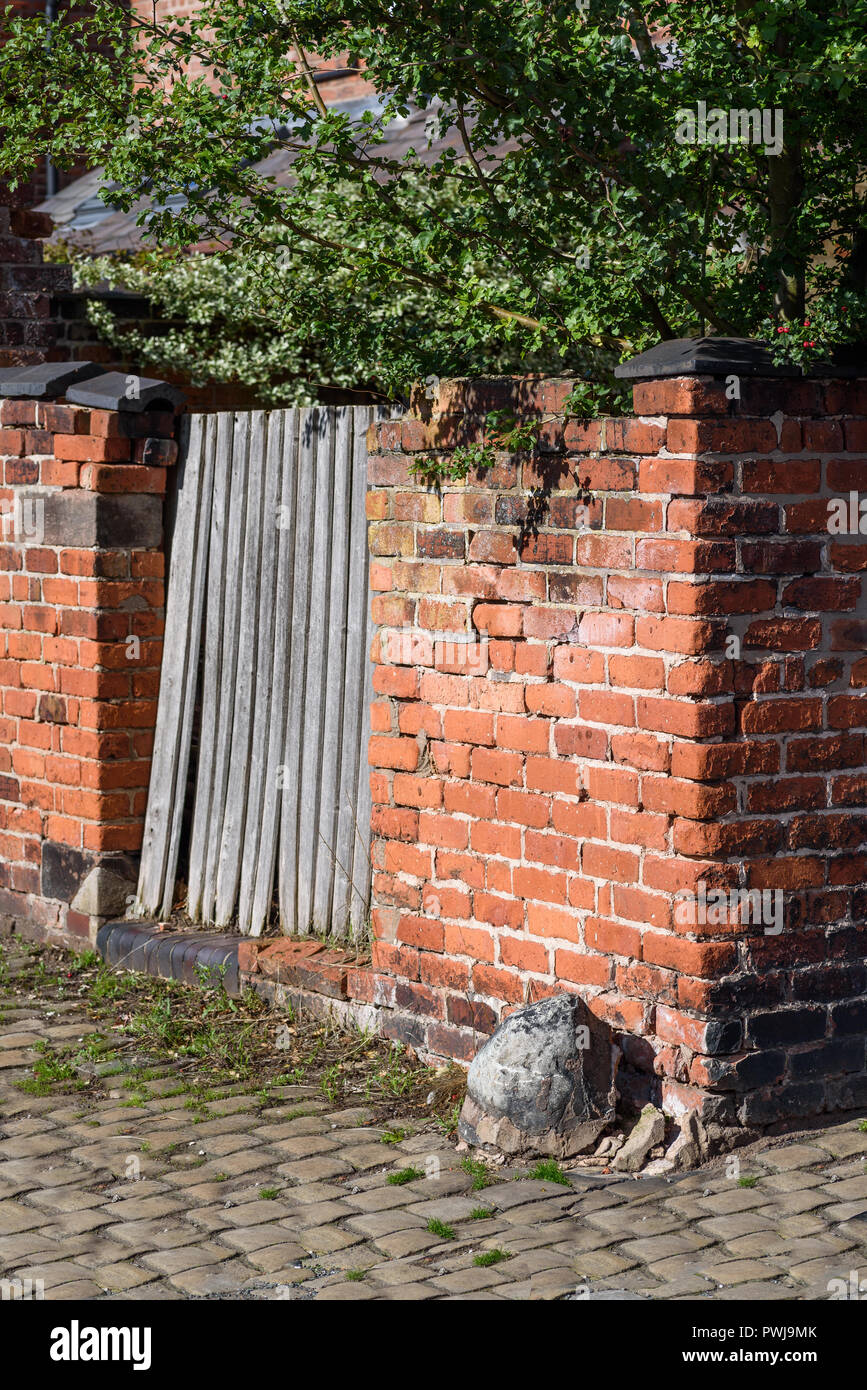 Corner of a traditional British Victorian terraced back alley with old brick wall, gate and cobblestones. Stock Photo