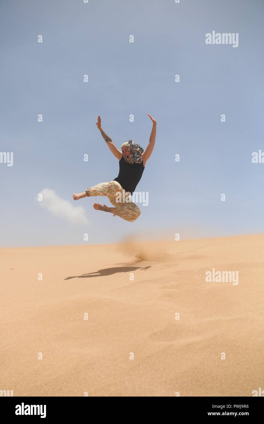 Woman in the desert jumping of a dune Stock Photo