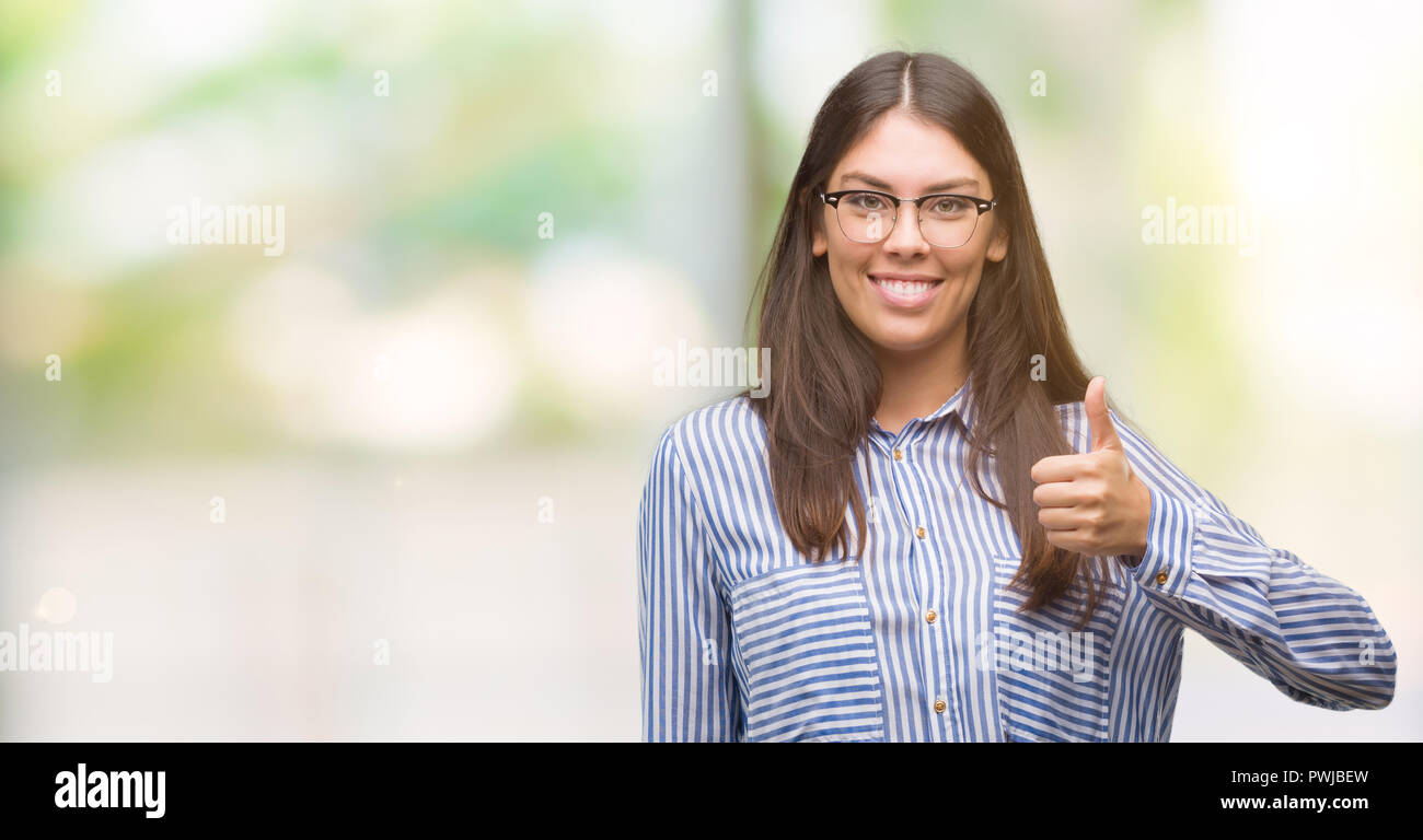 Young beautiful hispanic business woman doing happy thumbs up gesture ...