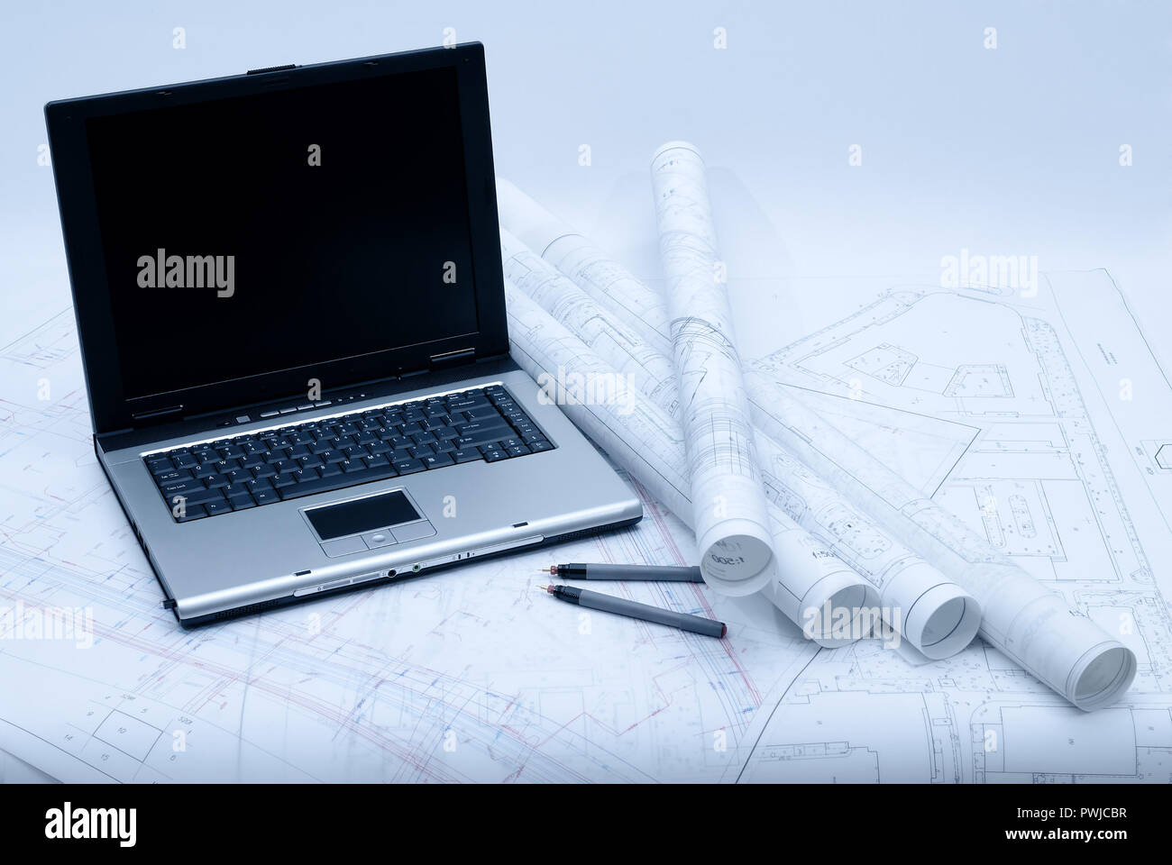 Computer with architectural plans lying on table. Picture in blue tint Stock Photo