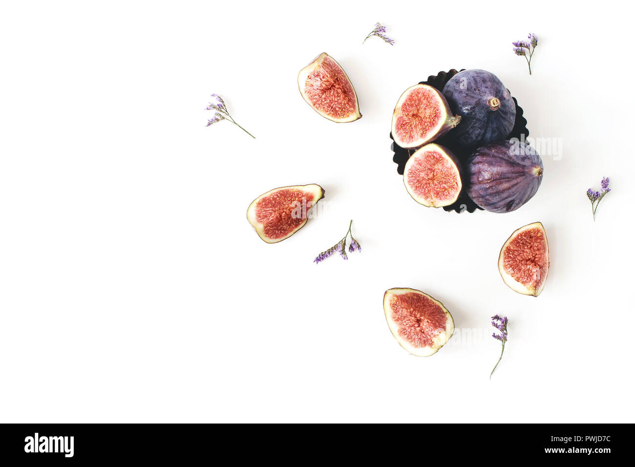 Fresh ripe purple figs composition. Food Photo. Sliced and whole exotic fruit in vintage bowl. Limonium flowers on a white table background. Floral pa Stock Photo