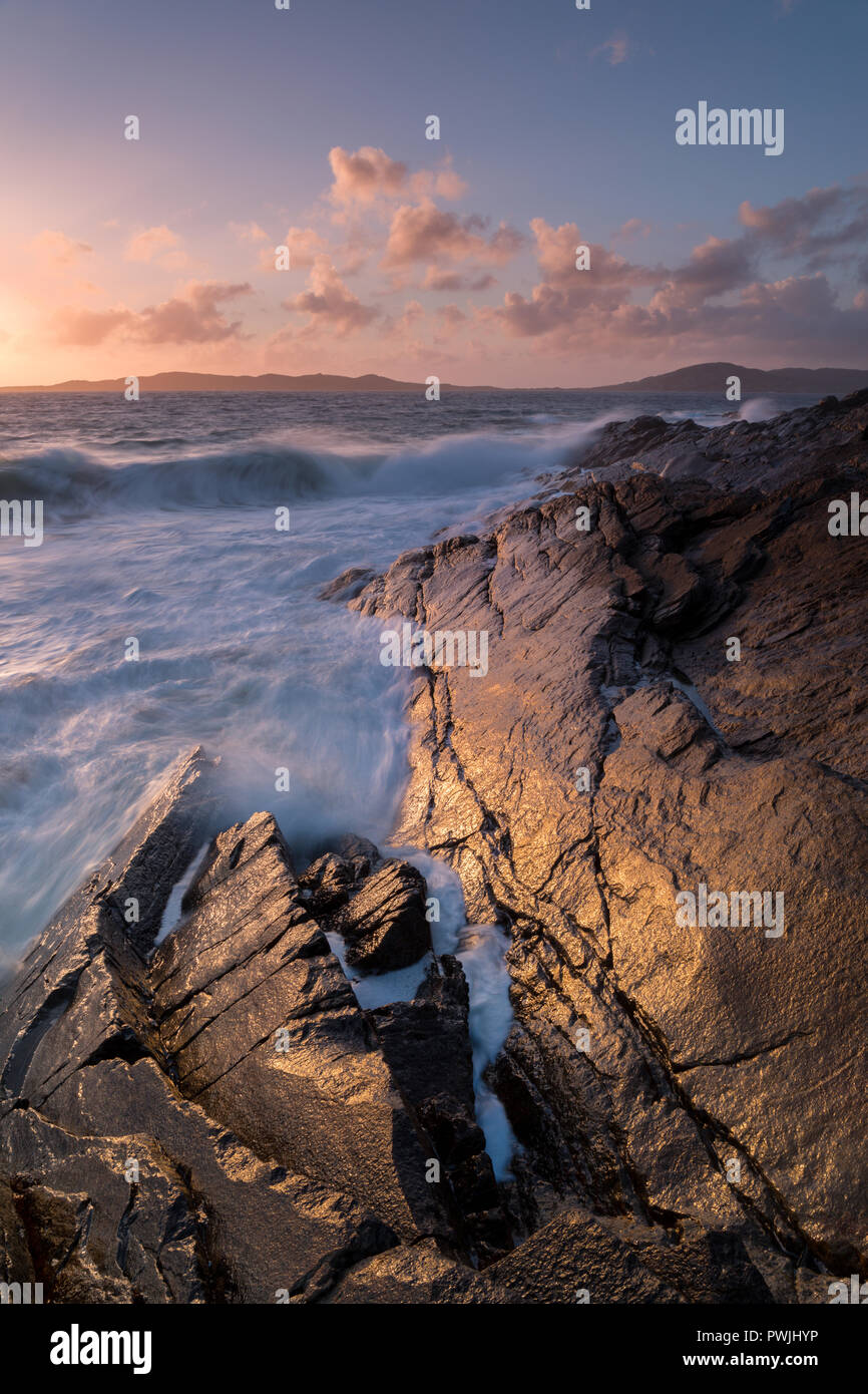 Waves breaking over wet rocks on Harris at sunset. Golden light on the rocks Stock Photo