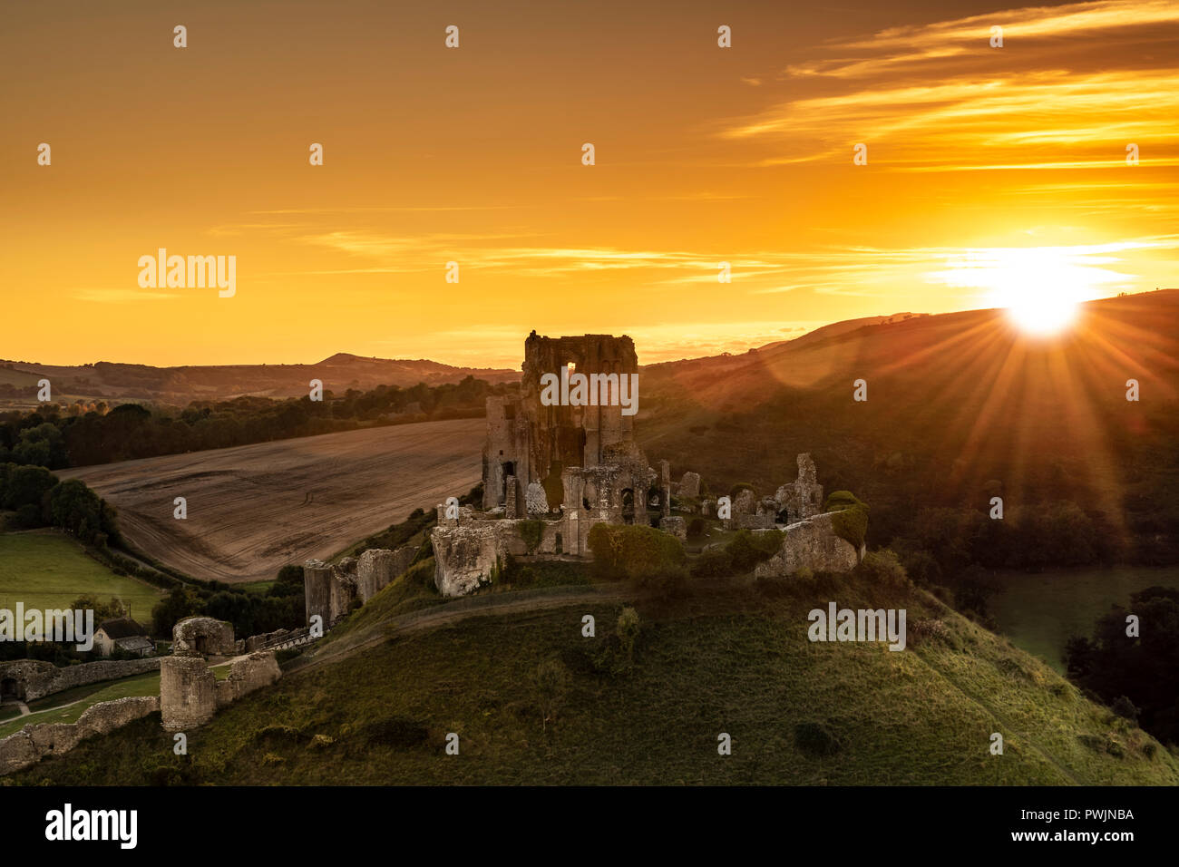 The sun sets behind the Purbeck Hills in Dorset as Corfe Castle fades in the last rays of late September sunshine. Stock Photo