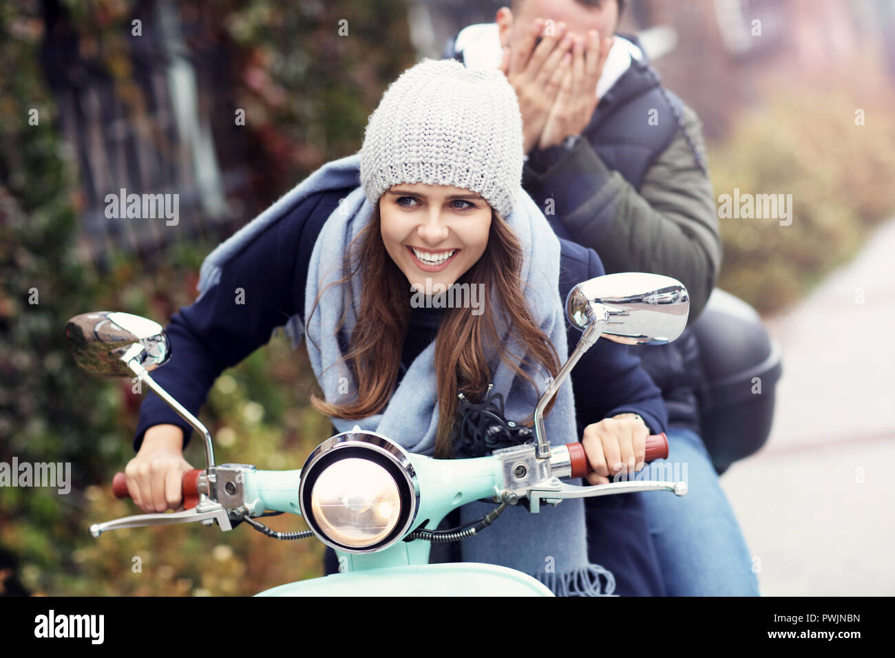 Picture of beautiful young couple smiling while riding scooter in city in autumn Stock Photo
