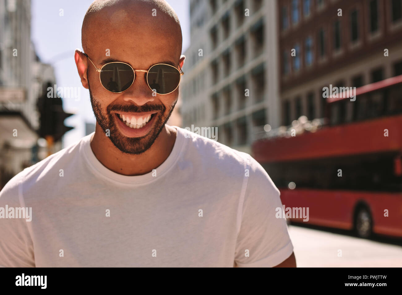 Close up portrait of handsome young man wearing sunglasses walking down the street and smiling. African man being a tourist in a big city. Stock Photo