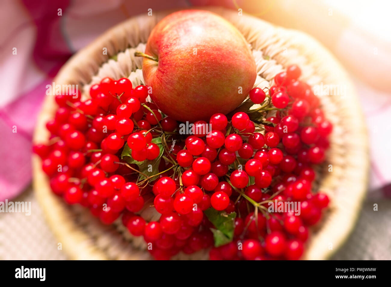 Ripe red apple and a sprig of viburnum with berries on a round wicker plate Stock Photo