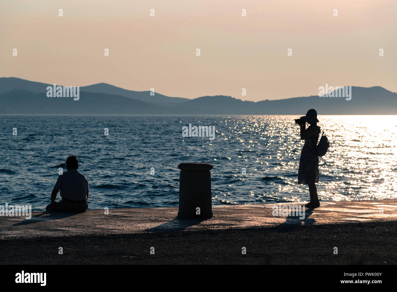 Couple of silhouetted tourists by the sea with a camera muted tones Stock Photo