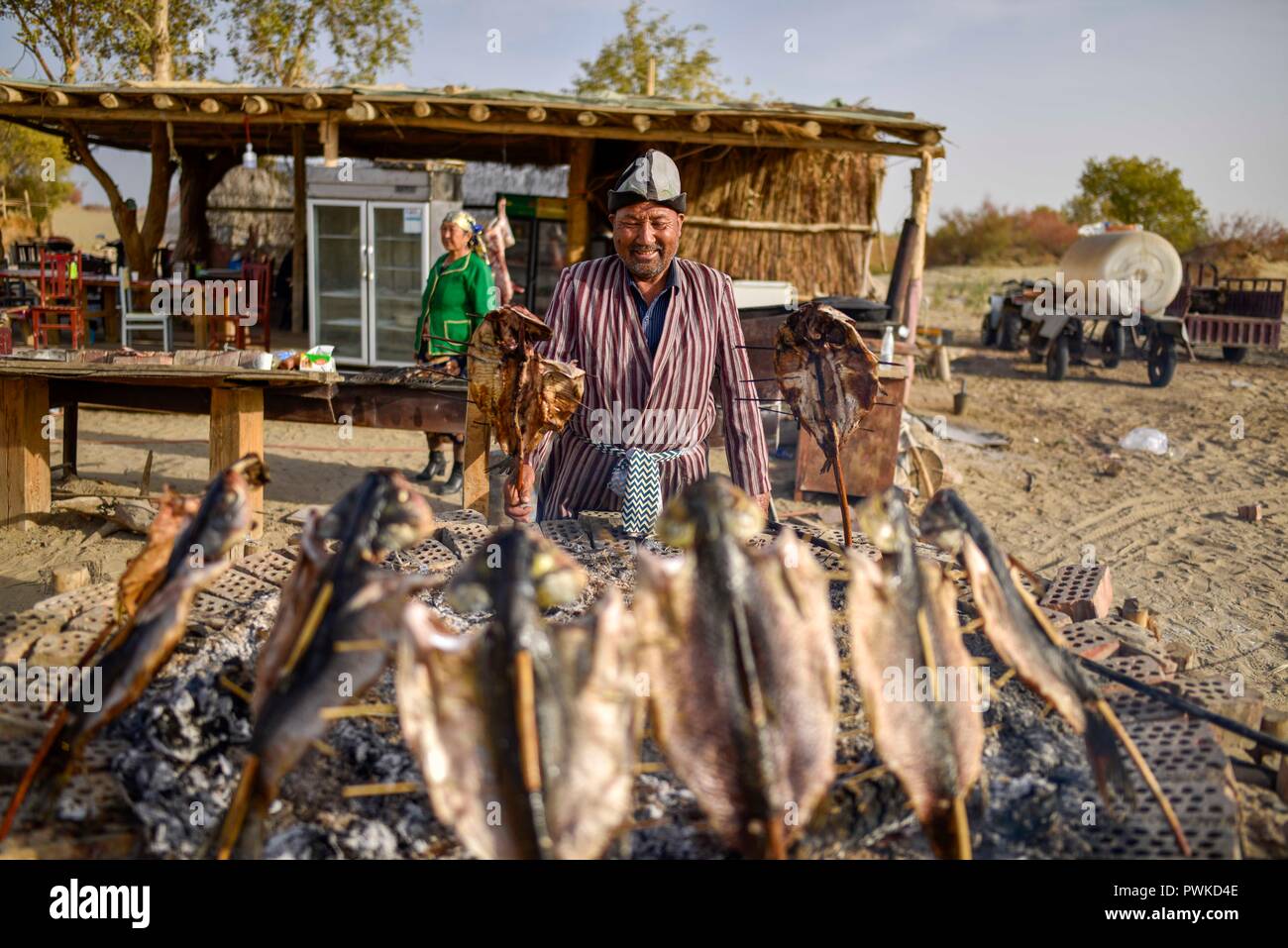 (181017) -- YULI, Oct. 17, 2018 (Xinhua) -- A resident makes roast fish at the Lop Nur People Village of Yuli County, northwest China's Xinjiang Uygur Autonomous Region, Oct. 16, 2018. The Lop Nur people depended basically on fishing for livelihood and developed a distinct culture based on their special lifestyle. Located in Tarim basin, Yuli is known for its natural scenery and ethnic culture and keeps attracting numerous tourists from at home and abroad. From Oct. 1 to 16, 2018, Yuli County has received more than 230,000 visitors, with a year-on-year increase of 31.46 percent. (Xinhua/Zhao G Stock Photo