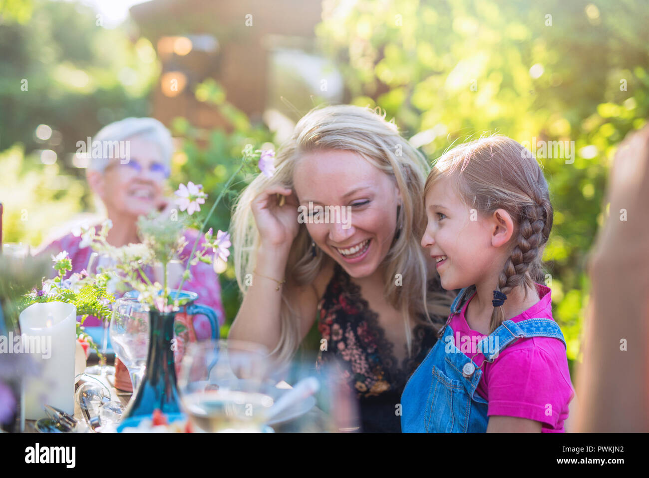 Summertime. a family of three generations gathered around a table in the garden to share a meal. Focus on complicity moment between a young mother and Stock Photo